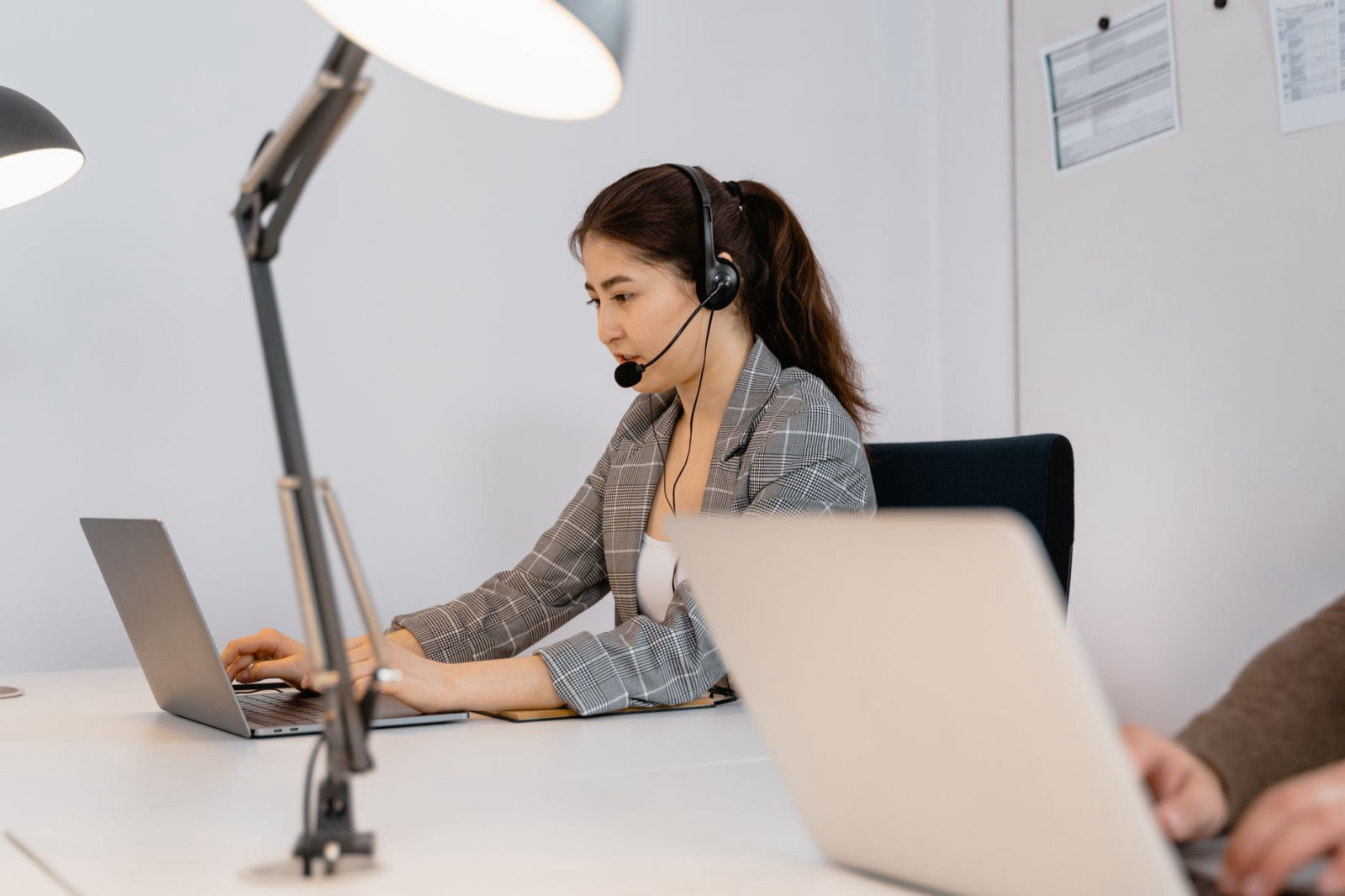 A professional woman wearing a headset works on a laptop at a modern office desk — illustrating a done for you AI voice agent for small business Santa Clarita