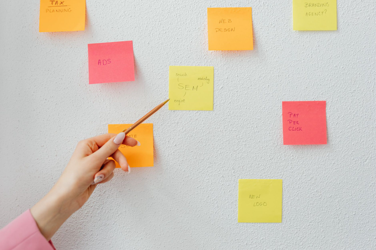 A hand pointing to colorful sticky notes on a wall organized with small business marketing ideas including SEO, ads, web design, and pay-per-click