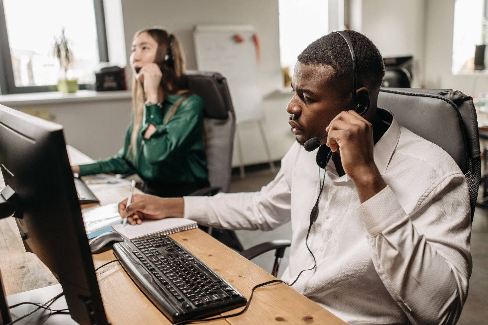 A focused call center agent with a headset answers customer calls at his desk, illustrating how does an AI answering service work for heating and cooling companies by ensuring every call is captured and dispatched efficiently